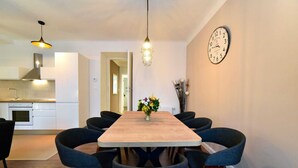 A dining area with a wooden table and six chairs, a clock on the wall, and a kitchen in the background. - Moin - Moin Apartment and Suite Zagreb (Zagreb)