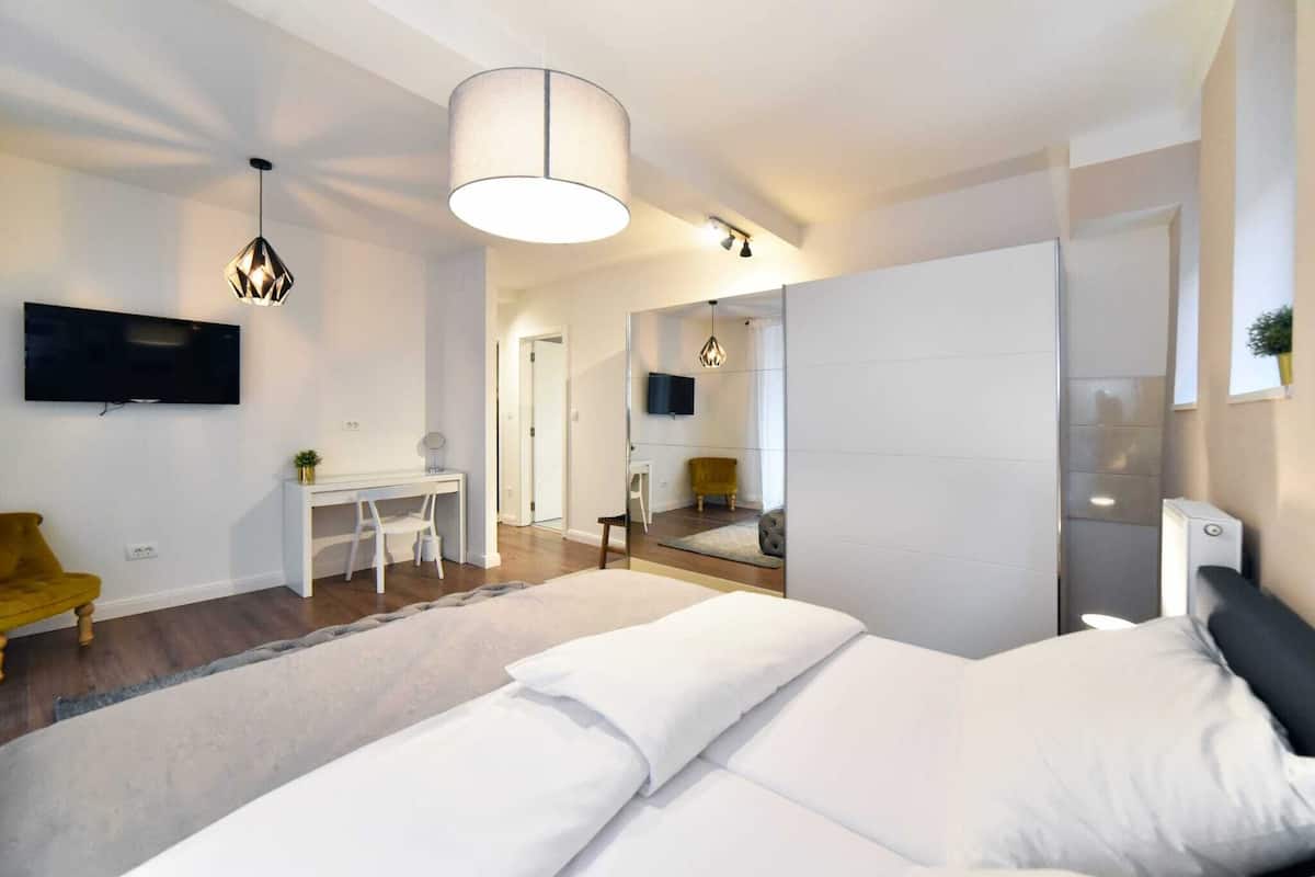 A modern bedroom with a large bed, a desk, a chair, and a TV mounted on the wall.