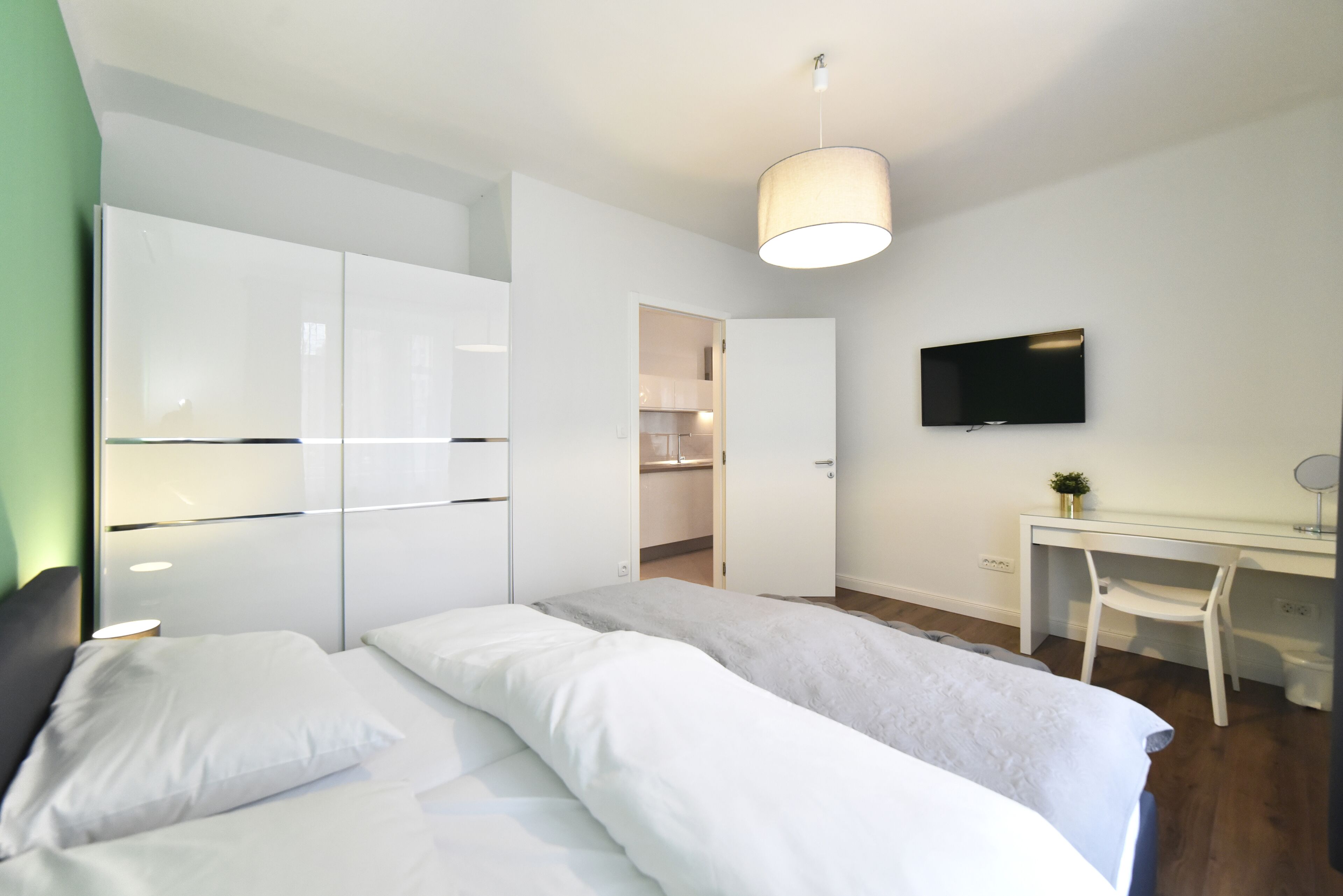 A modern bedroom with a bed, a desk, and a TV.