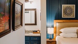 A bedroom with a wooden ceiling, a bed with white bedding, a nightstand with a lamp, a dresser with blue cabinets, and a framed picture on the wall.