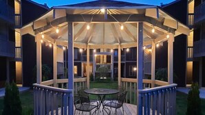 A covered outdoor seating area with a table and chairs, surrounded by a wooden deck and a glass enclosure.