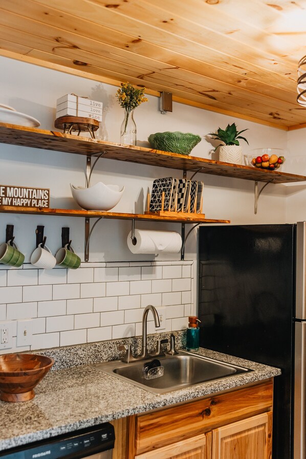 Une cuisine avec des meubles de rangement en bois, un plan de travail en granit, un évier en acier inoxydable et un réfrigérateur noir.