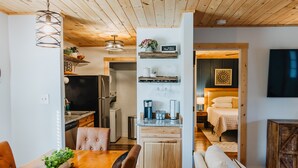 A modern kitchen with a dining area, a living room with a sofa, and a bedroom with a bed and nightstand.