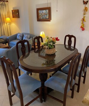 Uma mesa de jantar com seis cadeiras, tampo de vidro e um arranjo floral.