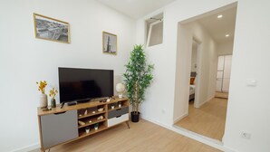Una sala de estar moderna con televisor de pantalla plana, mueble de entretenimiento de madera, plantas en macetas e imágenes enmarcadas en la pared.