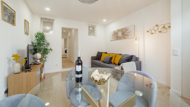 Una sala de estar moderna con una mesa de centro de vidrio, sofás grises y un elemento decorativo en la pared.