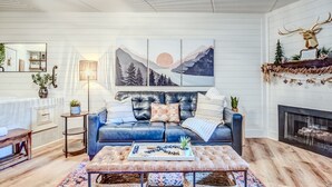 A cozy living room with a blue leather sofa, a coffee table with decorative items, a fireplace, and a wall-mounted deer head decoration.