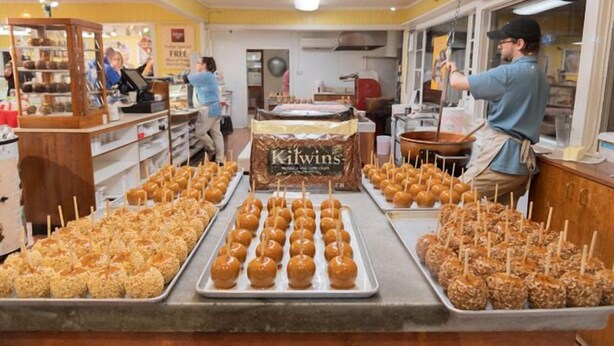 A bakery with trays of caramel apples and a sign for 'Kilwins'.