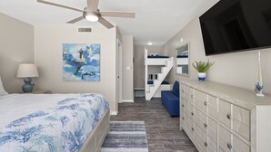 Un dormitorio con cama, ventilador de techo, televisión, escalera y baño.