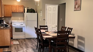 Un comedor con mesa y sillas de madera, un refrigerador blanco, estufa y armarios de madera.