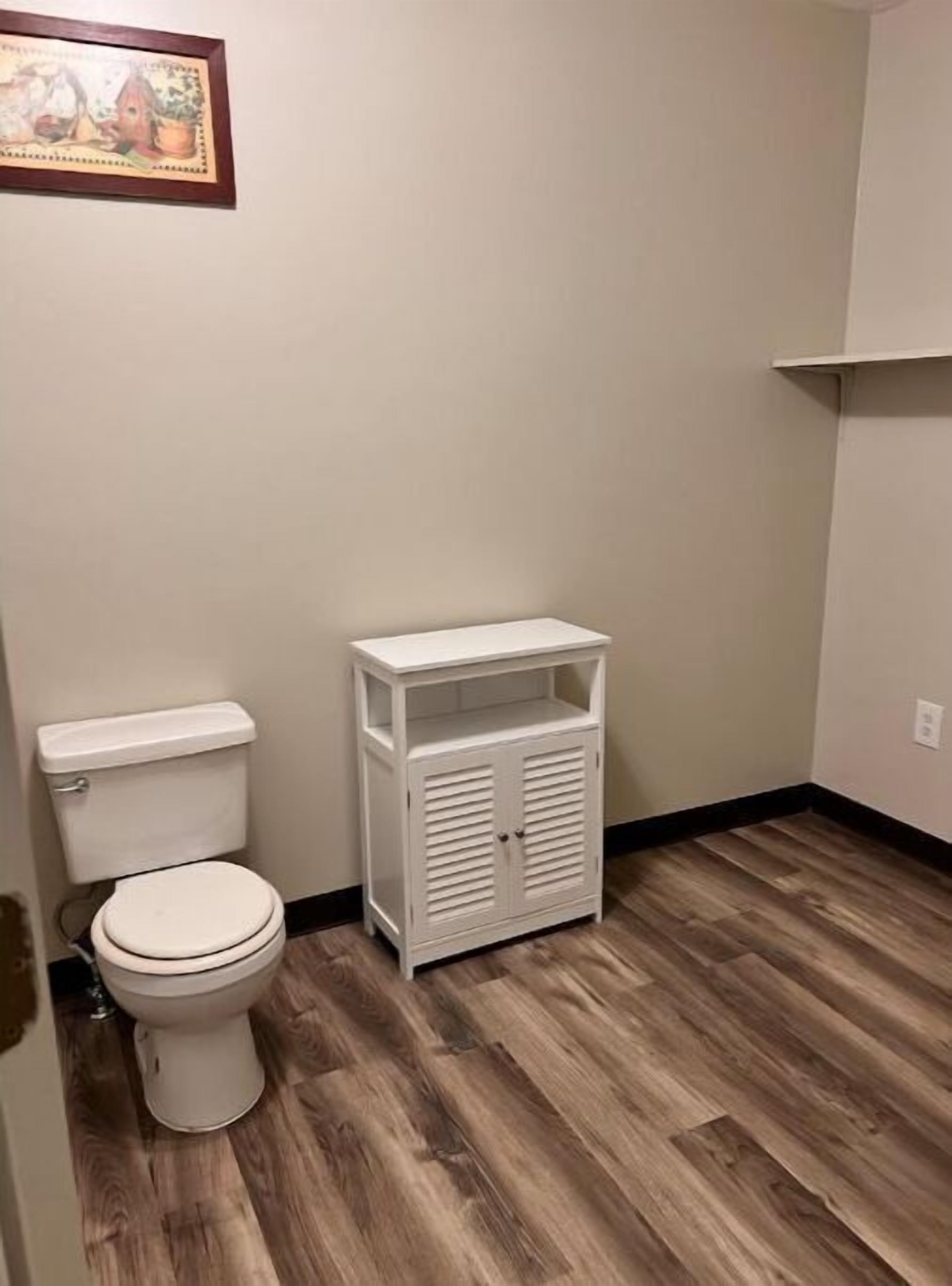 Une petite salle de bain avec des toilettes, un meuble blanc et un plancher en bois.