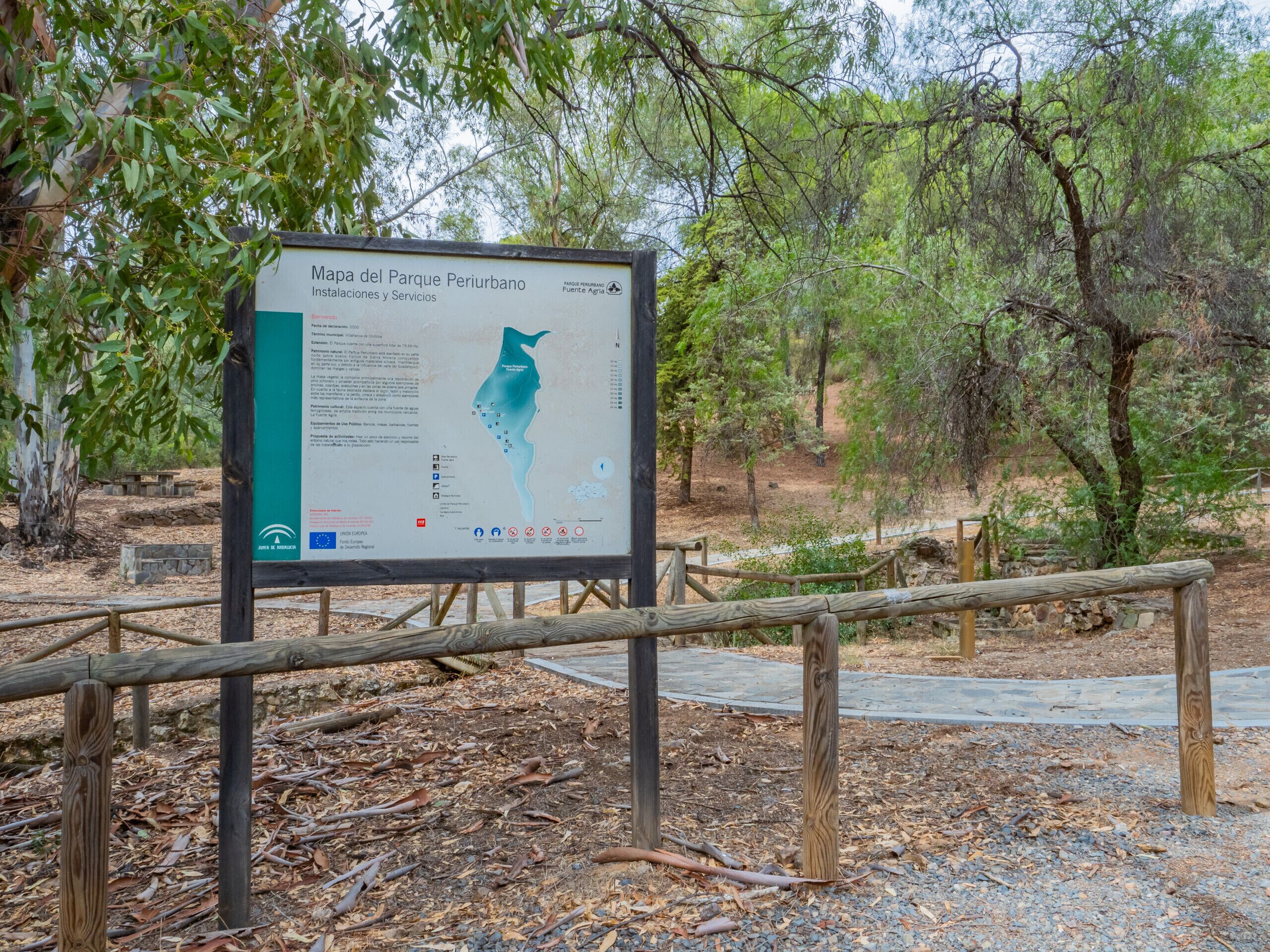 A signboard with a map and text, surrounded by trees and a wooden fence.