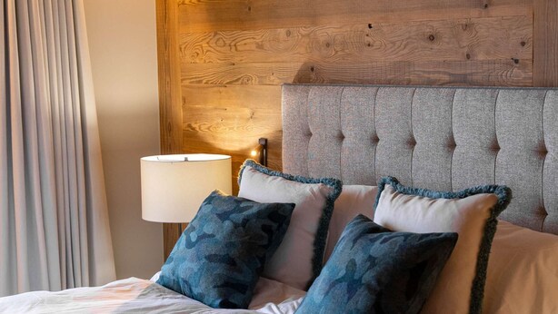 Une chambre d’hôtel avec une tête de lit en bois, un lit recouvert de draps blancs et une lampe sur une table de chevet.