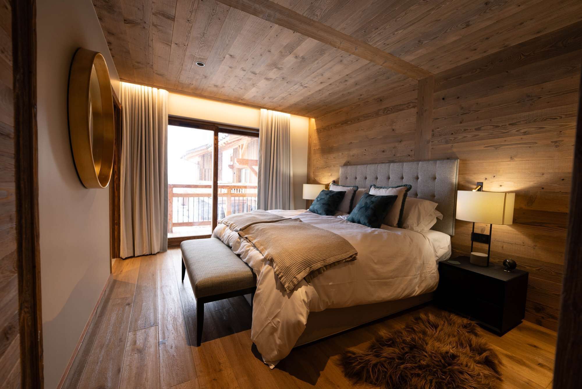Une chambre à coucher avec un grand lit, un banc, un plancher en bois, un tapis en fourrure et une table de chevet avec une lampe.