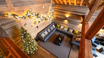 A cozy loft-style living area with a wooden ceiling, a sectional sofa, a small coffee table, and a Christmas tree.