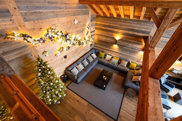 A cozy loft-style living area with a wooden ceiling, a sectional sofa, a small coffee table, and a Christmas tree.