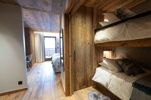 A wooden interior with bunk beds, a visible door leading to a balcony, and a hallway.