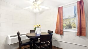 Un coin repas comprenant une table ronde, quatre chaises, un ventilateur de plafond et une fenêtre avec des rideaux.