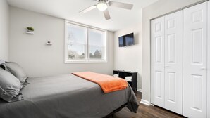 Une chambre à coucher avec un lit, un ventilateur de plafond, une fenêtre, un téléviseur et une armoire.