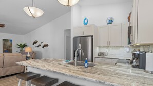 A modern kitchen with a marble countertop, stainless steel appliances, and a bar area with stools. - Brand new August 2023 3 BR, 2 BA Tarpon on stilts (Homosassa)