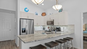 A modern kitchen with white cabinets, stainless steel appliances, a marble countertop, and bar stools. - Brand new August 2023 3 BR, 2 BA Tarpon on stilts (Homosassa)