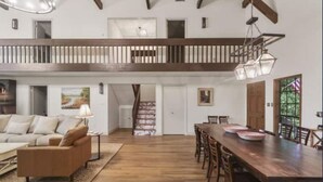 Amplia zona de estar tipo loft con una escalera de madera, una mesa de comedor con sillas y un sofá.