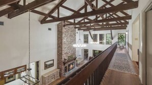 Un pasillo espacioso con vigas de madera a la vista, chimenea de piedra y vistas al exterior.