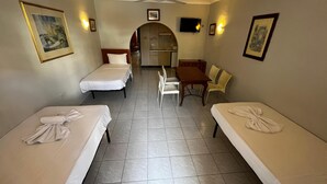 A hotel room with two single beds, a small dining table, a chair, a kitchenette, and a ceiling fan. - Cozy poolside apartment with 5 beds (San Pawl il-Baħar)