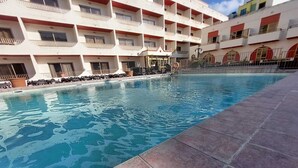 A swimming pool with tiled edges, surrounded by a multi-story building with balconies and a covered seating area. - Cozy poolside apartment with 5 beds (San Pawl il-Baħar)