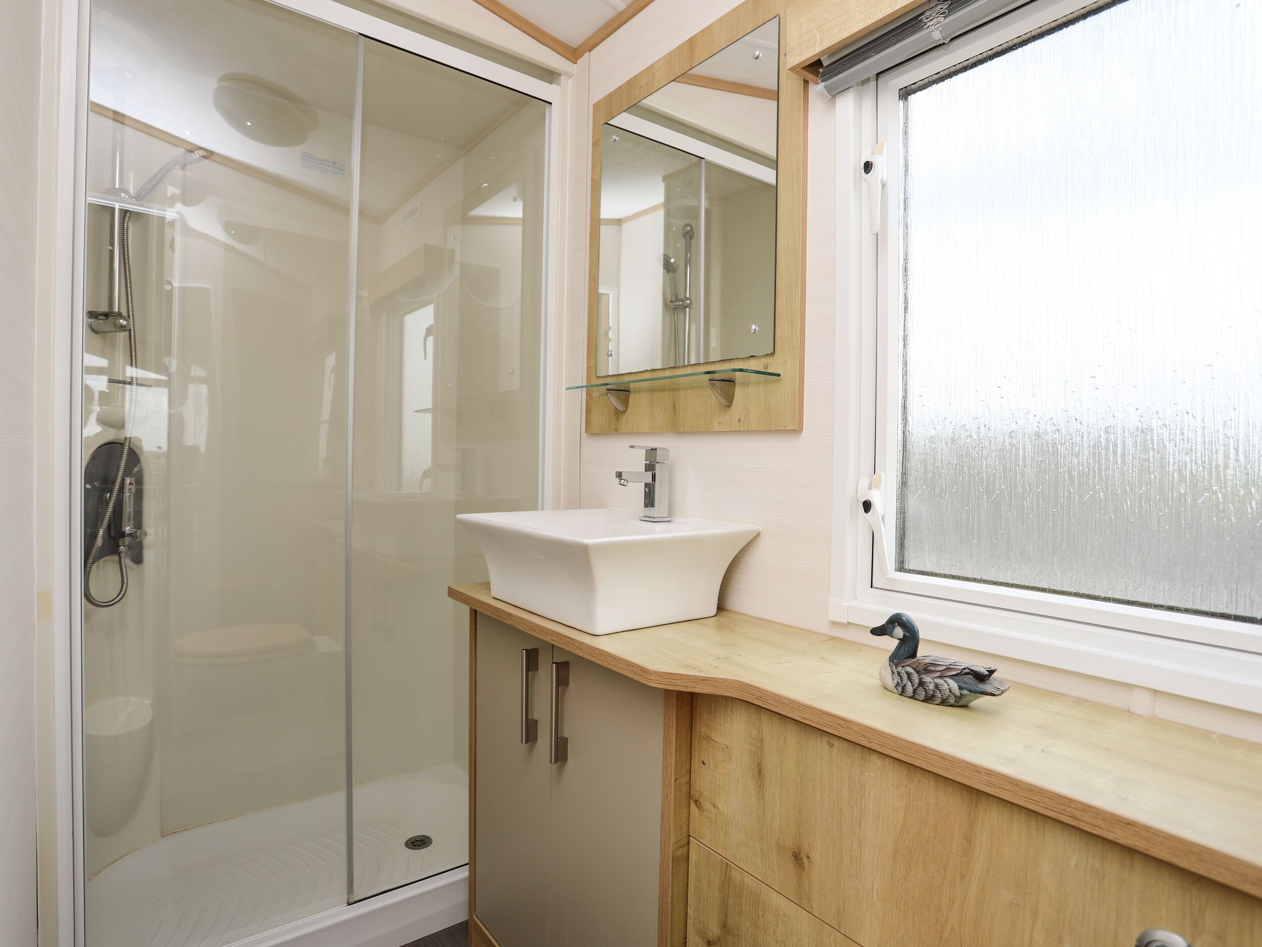 Un baño moderno con ducha envuelta en vidrio, un lavamanos blanco y un mueble de tocador de madera.