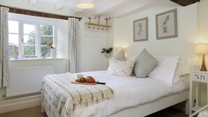 Quarto com cama, janela com cortinas, mesa de cabeceira com abajur e quadros na parede.