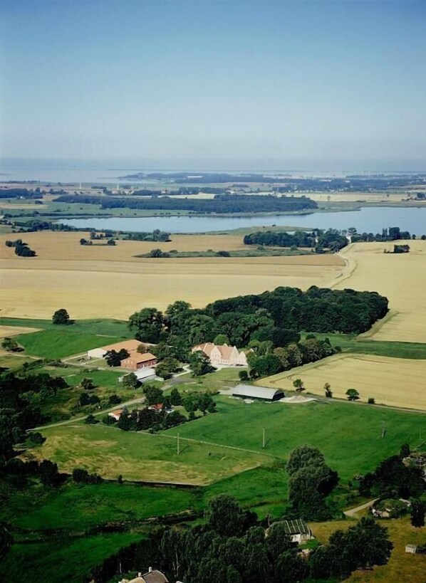 Vista aérea de un paisaje rural con campos, un lago y un pequeño grupo de edificios que incluye una casa blanca y un granero rojo.