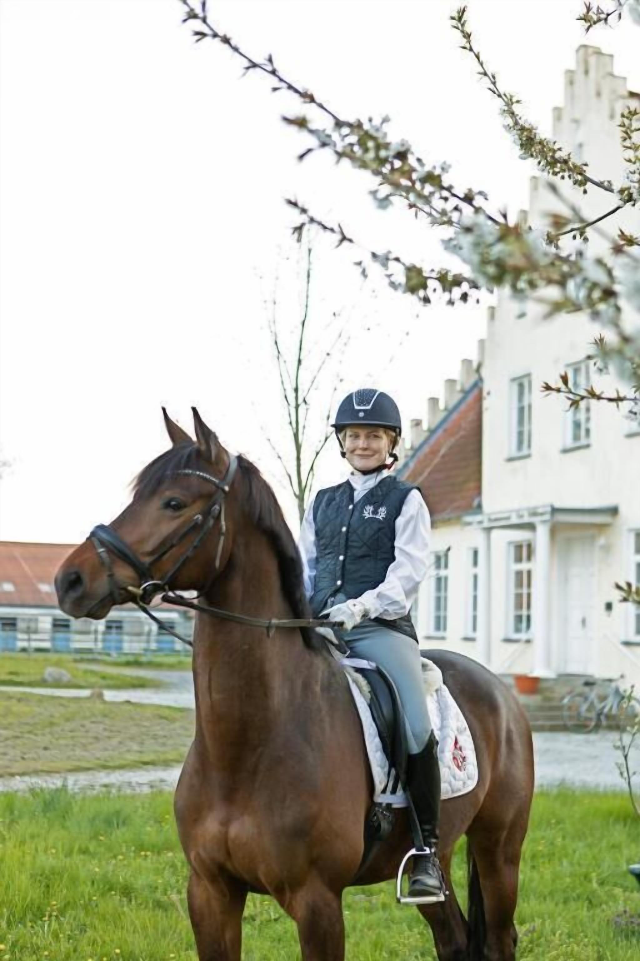 A person riding a horse in a grassy area with a building in the background.