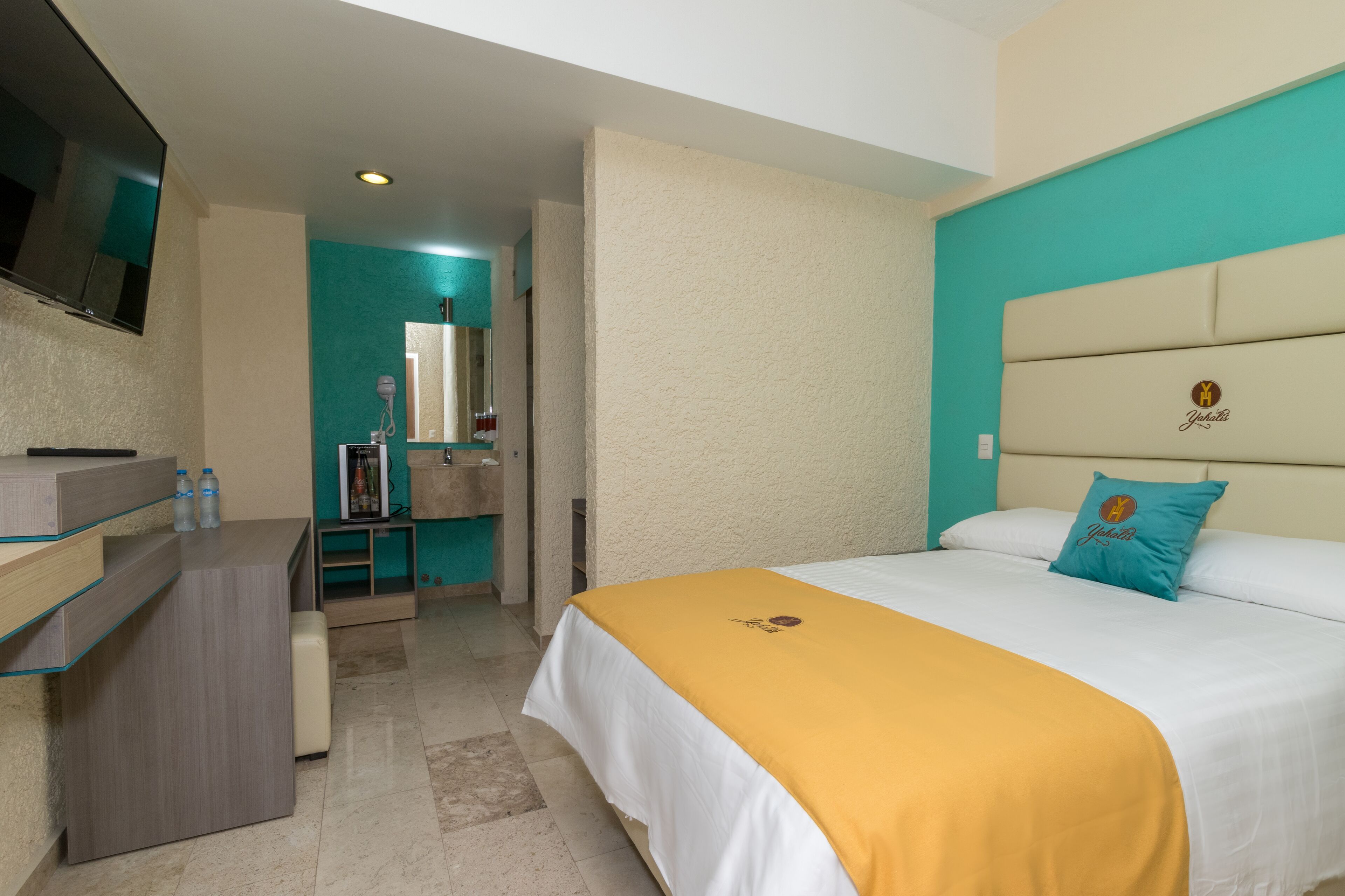 Une chambre d’hôtel avec un lit, un bureau, un miroir et une télévision.