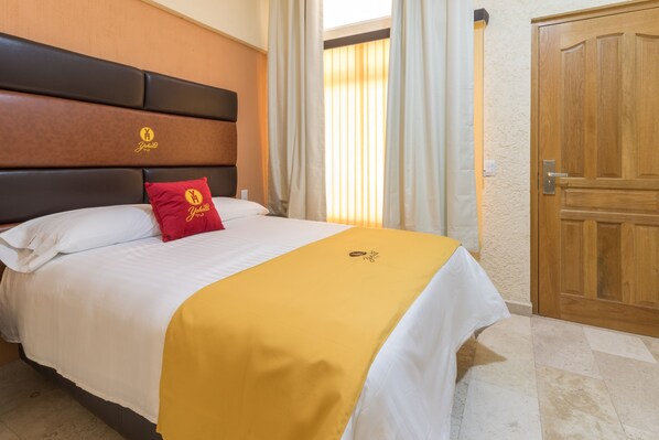 Une chambre d’hôtel avec un lit, une tête de lit en bois, un oreiller rouge, une couvre-lit jaune et une porte en bois.