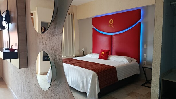 Una camera d'hotel moderna con un ampio letto, una parete di accentazione rossa e un originale design di specchio curvo.