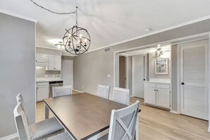 Un comedor con una mesa y sillas de madera, una araña y una cocina al fondo.