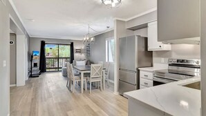 Una cocina moderna con electrodomésticos de acero inoxidable, un comedor con mesa y sillas, y un balcón con vistas.