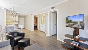 Una sala moderna con una televisión de pantalla plana, sillones de cuero, un comedor y una cocina al fondo.