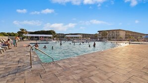 Zona de piscina con suelo de baldosas, una escalera de metal y un área de descanso cubierta.