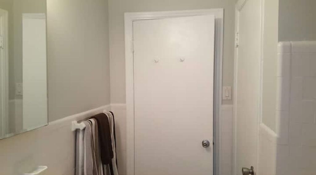 A bathroom with a white door, a towel rack with a towel, and a mirror on the wall.