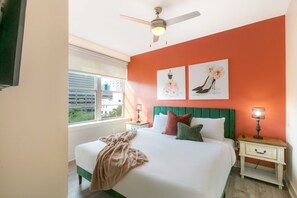 Un dormitorio con cama, mesita de noche, ventilador de techo y una obra de arte en la pared.