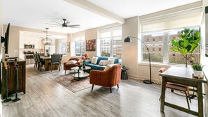 Un salon spacieux avec un canapé bleu, des fauteuils orange, une table à manger et une cuisine en arrière-plan.
