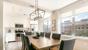 Une cuisine moderne avec des meubles blancs, des appareils en acier inoxydable et une grande table à manger entourée de six chaises.