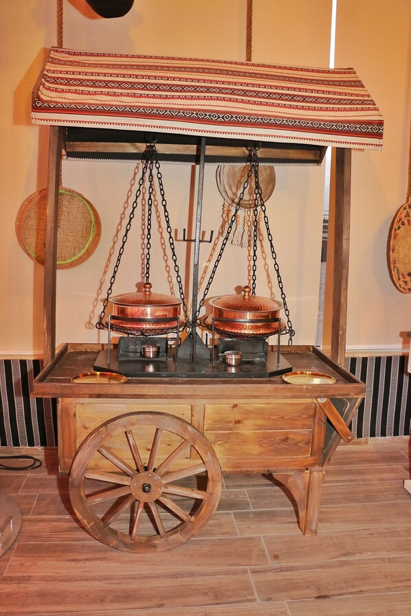 A traditional food cart with two copper pots, a wooden base, and a patterned canopy.