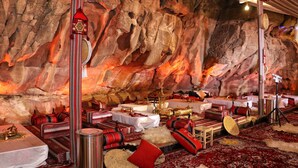 A room with a rock wall, tables set with traditional decor, and a large hanging ornament. - Rum Imagination Luxury Camp (Wadi Rum)
