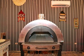 Un four à pizza en briques de la marque « Shanafield », installé dans une cuisine dont les murs sont recouverts d’un papier peint à rayures et décorée de tableaux.