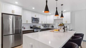 A modern kitchen with white cabinets, stainless steel appliances, and black pendant lights. - Outdoor Bar/Jacuzzi/Ocean & Bay Breeze Hideaway (Chula Vista)