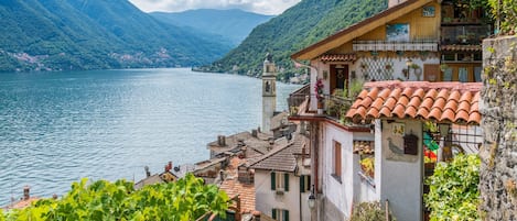 A coastal building with a bell tower, terracotta roof tiles, and a view of a lake and mountains.