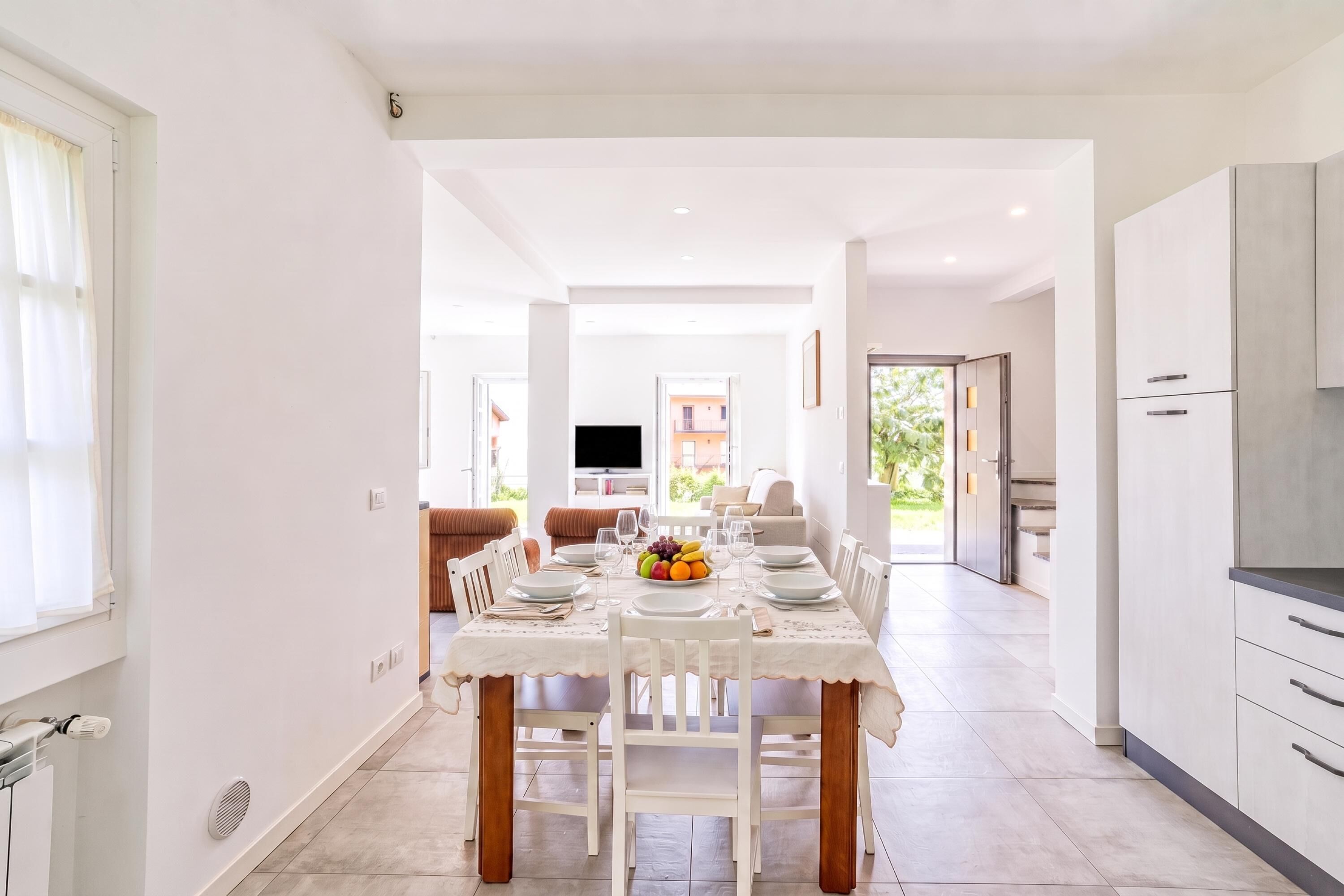 A modern dining area with a table set for four, a kitchen with cabinets, and a living area with a sofa and TV.